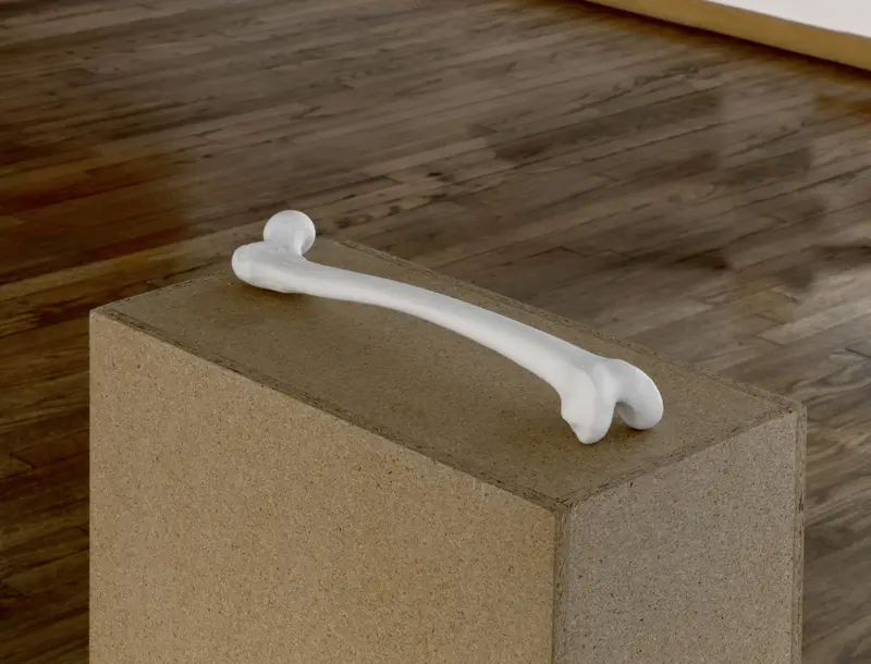 Zu sehen ist ein in Biskuitporzellan gegossener menschlicher Oberschenkelknochen platziert auf einem Sockel aus Sperrholz.